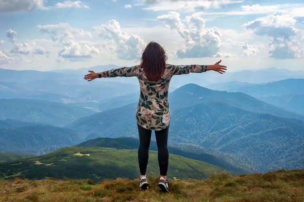 Ragazza che viaggia in montagna da sola, in piedi con le mani in alto raggiungendo la cima, accoglie un sole.