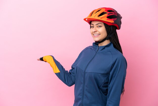 Ragazza ciclista adolescente isolata su sfondo rosa che estende le mani di lato per invitare a venire