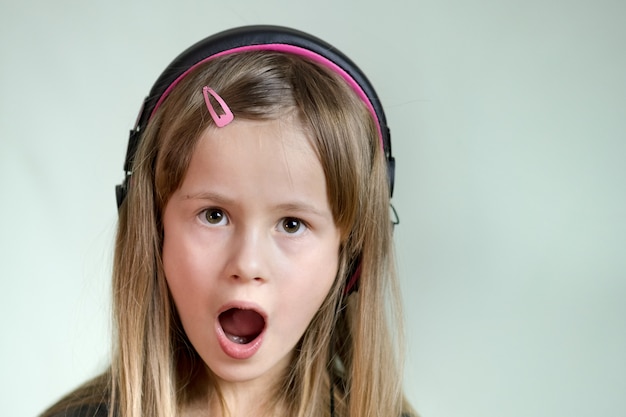 Ragazza cild sorridente graziosa che ascolta la musica in grandi cuffie rosa.