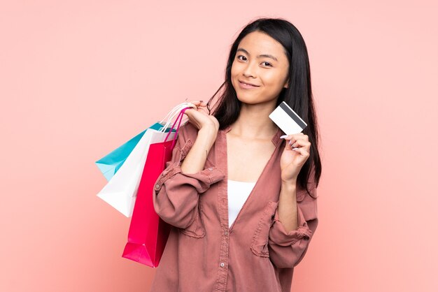 Ragazza cinese dell'adolescente isolata sui sacchetti della spesa rosa della tenuta e una carta di credito