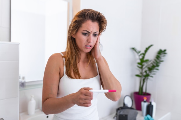 Ragazza colpita con la gravidanza indesiderata che guarda il test nel bagno.