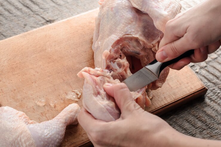 Ragazza coltella un pollo crudo a pezzi su un tagliere.
