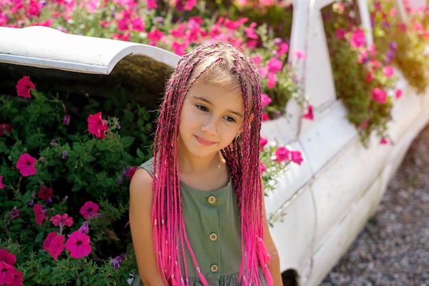 Ragazza con afropigtails rosa è in piedi vicino a un'aiuola in fiore con petunie