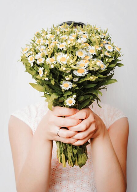 Ragazza con bouquet di camomilla al muro bianco