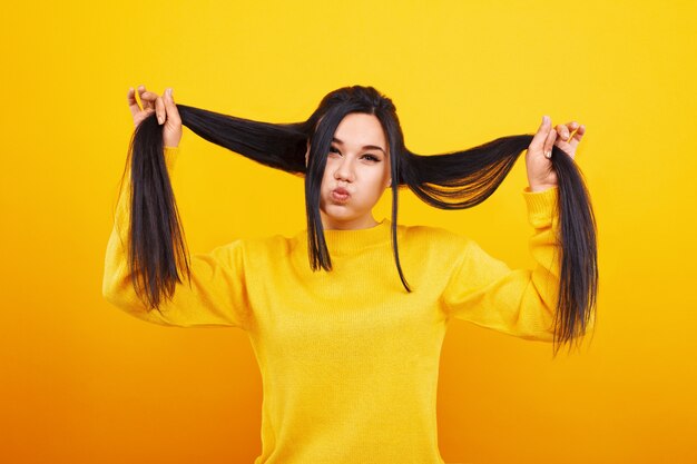 Ragazza con capelli lunghi, in maglione giallo che scherza sullo spazio giallo