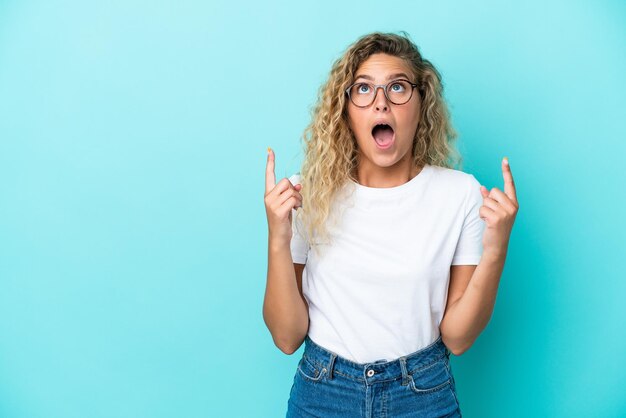 Ragazza con capelli ricci isolata su sfondo blu sorpresa e rivolta verso l'alto