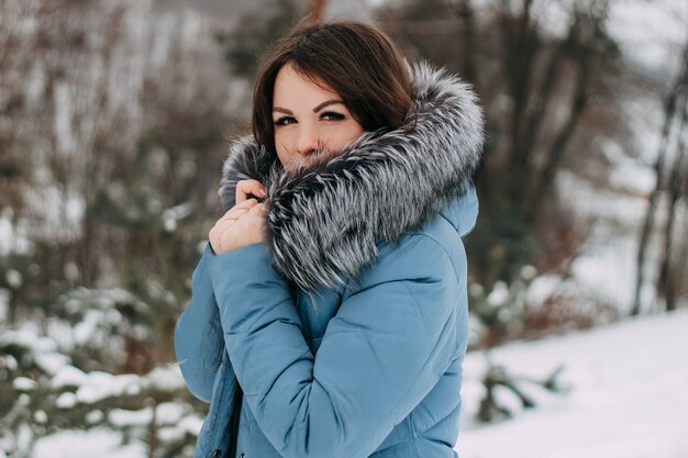 Ragazza con capelli scuri con pelliccia di volpe argentata naturale in posa in una foresta innevata.