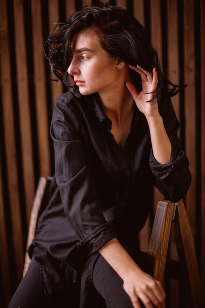 Ragazza con capelli scuri ricci e trucco naturale seduto su una sedia in pelle elaborazione di foto d'epoca