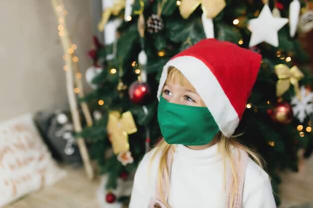 Ragazza con cappello e maschera di Babbo Natale, periodo natalizio, isolamento durante le vacanze, covid-19, coronavirus.