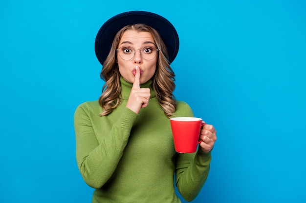 ragazza con cappello e occhiali tenendo la tazza isolata sul blu