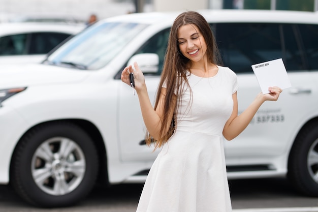 Ragazza con chiavi e accordo sullo sfondo della concessionaria auto