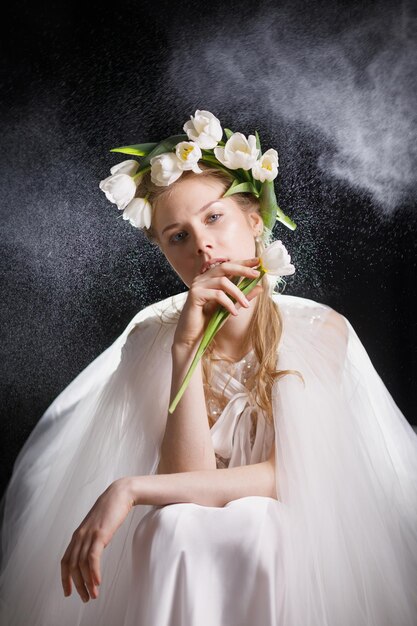 Ragazza con fiori bianchi sulla testa e nelle sue mani tulipani bianchi