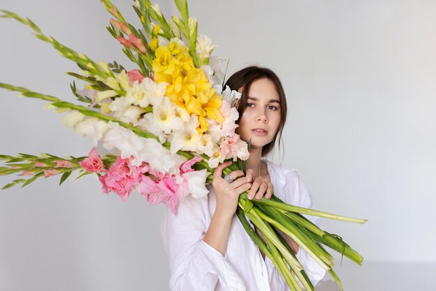 ragazza con fiori di gladioli in abiti bianchi su uno sfondo bianco