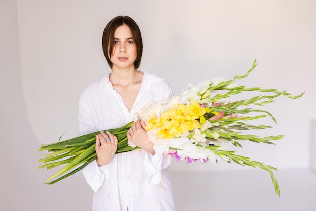 ragazza con fiori di gladioli in abiti bianchi su uno sfondo bianco