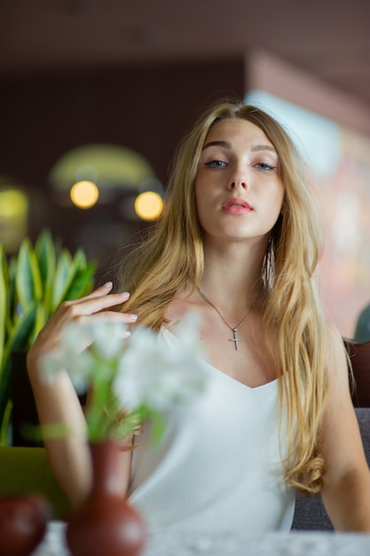 Ragazza con gli occhi azzurri che si siede sul caffè urbano. donna con acconciatura ondulata marrone. Concetto di stile di vita.