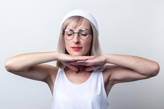 Ragazza con gli occhi chiusi che tiene le mani sotto il mento su uno sfondo chiaro