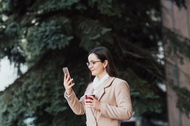 ragazza con gli occhiali e la tazza di caffè utilizza un telefono