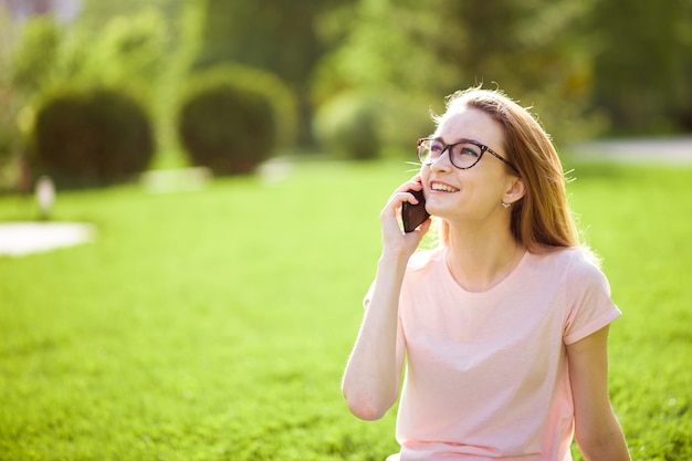 Ragazza con gli occhiali, parlando al telefono all'aperto. copia spazio.