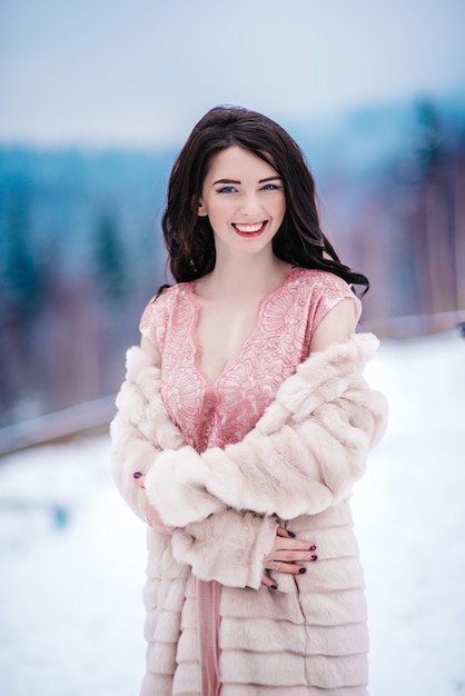 Ragazza con i capelli castani, gli occhi azzurri e un vestito rosa sullo sfondo delle montagne invernali