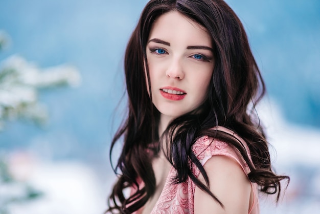 Ragazza con i capelli castani, gli occhi azzurri e un vestito rosa sullo sfondo delle montagne invernali
