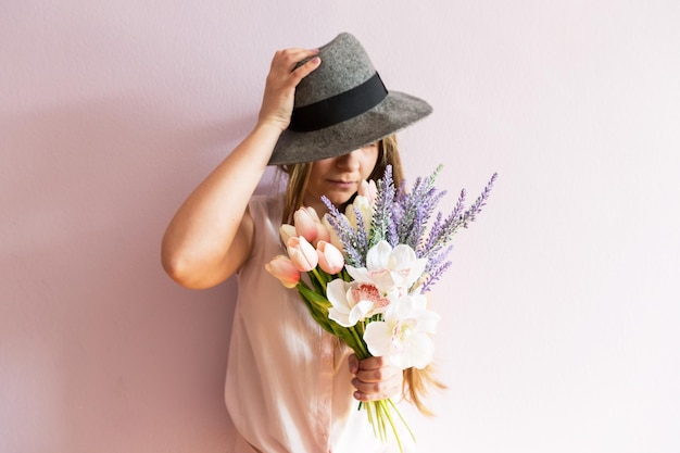 ragazza con i capelli lunghi biondi sciolti un cappello di feltro in testa tiene i fiori di primavera nelle sue mani