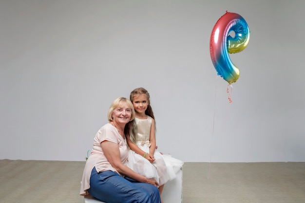 Ragazza con i capelli lunghi in abito festivo con la sua nonna anziana sfondo bianco famiglia studio girato