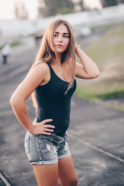 Ragazza con i capelli lunghi in posa per strada al tramonto Ragazza con un bel colore della pelle guarda di lato