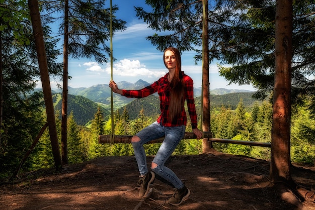 Ragazza con i capelli lunghi sull'oscillazione della foresta con splendida vista sulle montagne