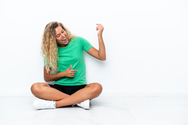 Ragazza con i capelli ricci che si siede sul pavimento che fa il gesto della chitarra