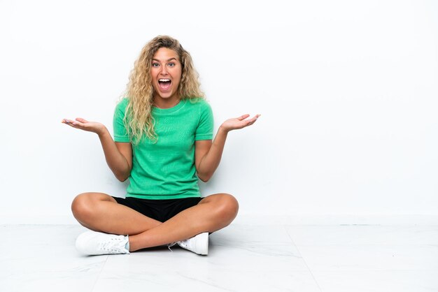 Ragazza con i capelli ricci che si siede sul pavimento con l'espressione facciale scioccata