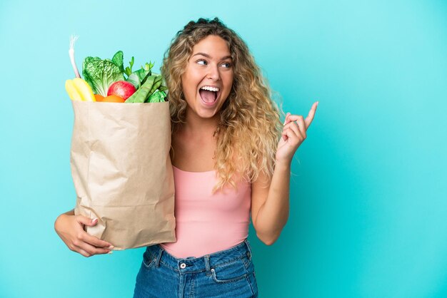 Ragazza con i capelli ricci che tiene un sacchetto della spesa isolato su sfondo verde con l'intenzione di realizzare la soluzione sollevando un dito