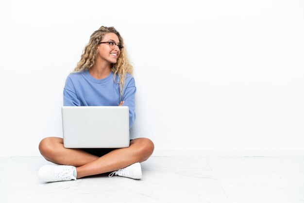 Ragazza con i capelli ricci con un laptop seduto per terra in posizione laterale