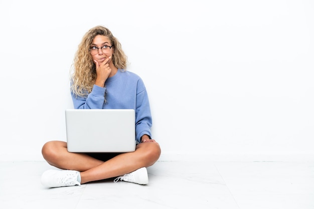 Ragazza con i capelli ricci con un laptop seduto sul pavimento con dubbi e con un'espressione del viso confusa