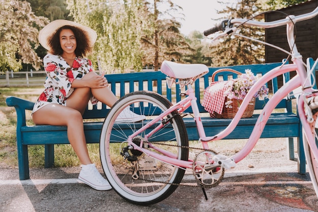 Ragazza con i capelli ricci è seduto sulla panchina accanto alla bicicletta