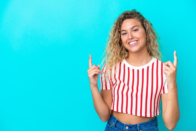 Ragazza con i capelli ricci isolata su sfondo blu che indica una grande idea