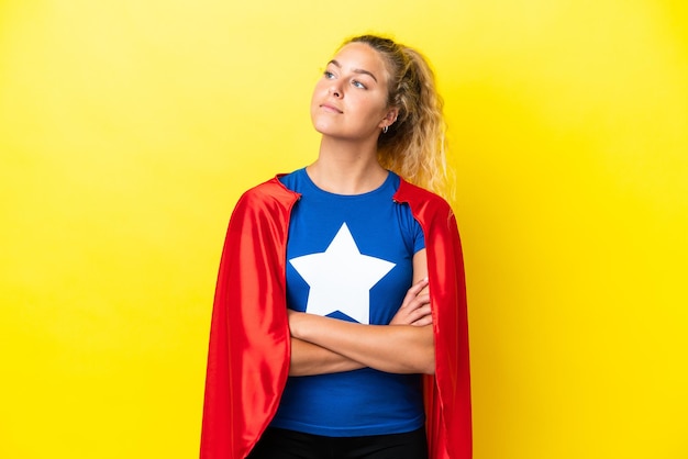 Ragazza con i capelli ricci isolata su sfondo giallo in costume da supereroe con le braccia incrociate