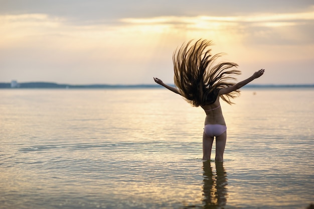 Ragazza con i capelli sciolti sul mare durante il tramonto