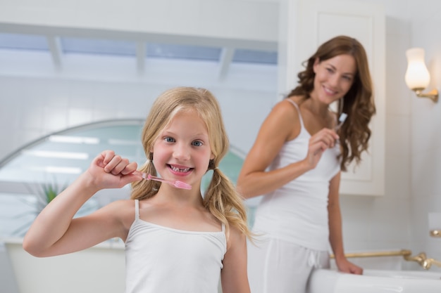 Ragazza con i denti di spazzolatura della madre in bagno