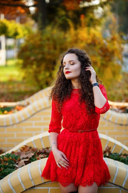 Ragazza con i riccioli in un vestito rosso in un vicolo della città autunnale