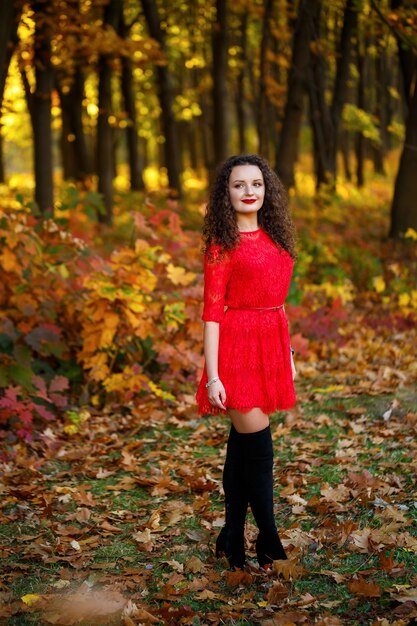 Ragazza con i riccioli in un vestito rosso nella foresta autunnale