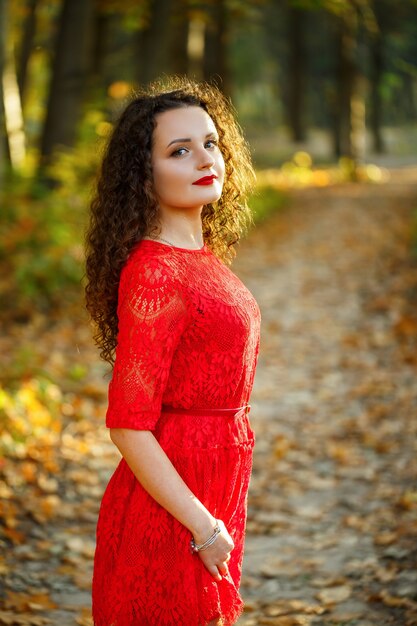 Ragazza con i riccioli in un vestito rosso nella foresta autunnale