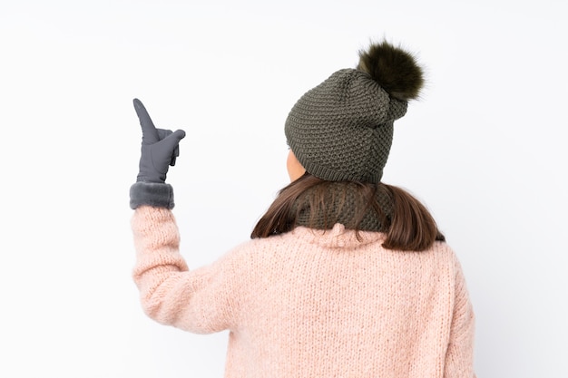 Ragazza con il cappello di inverno che indica indietro con il dito indice