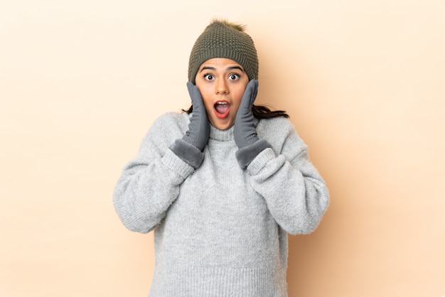 Ragazza con il cappello di inverno sulla parete beige con espressione facciale sorpresa