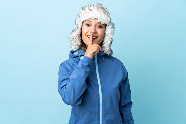 Ragazza con il cappello di inverno sulla parete blu che fa gesto di silenzio