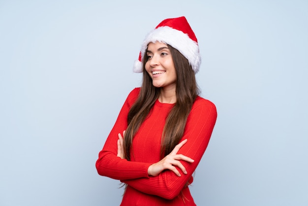 Ragazza con il cappello di natale sopra l'azzurro isolato che osserva al lato