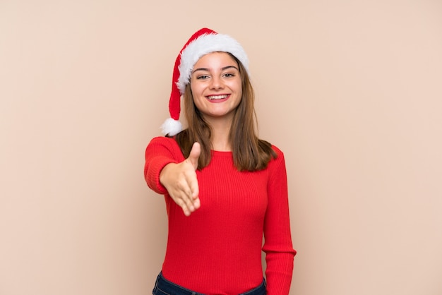 Ragazza con il cappello di natale sopra la stretta di mano isolata della parete dopo il buon affare