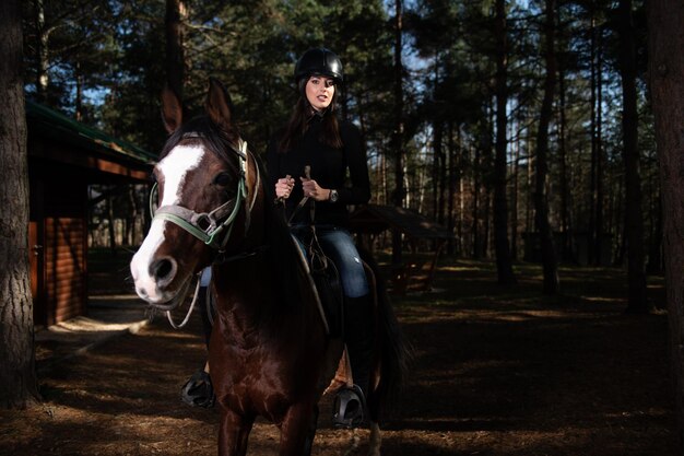 Ragazza con il casco che monta un cavallo nella foresta