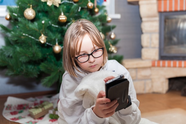 Ragazza con il cellulare all'albero di Natale