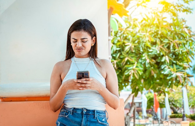 Ragazza con il cellulare che riceve un messaggio sgradevole Giovane donna con cellulare che legge un messaggio con una faccia sgradevole Ragazza turbata accigliata leggendo un messaggio sgradevole