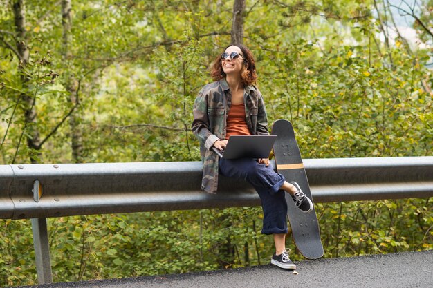 Ragazza con il computer seduto accanto allo skateboard